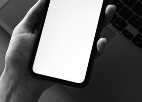 Servicios Monochrome photo of a smartphone held over a laptop for tech-themed design.