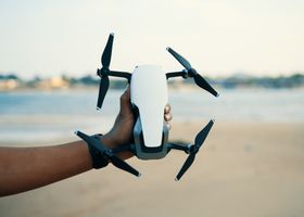 Close-up of a hand holding a drone on a beach during daytime, showcasing modern technology.